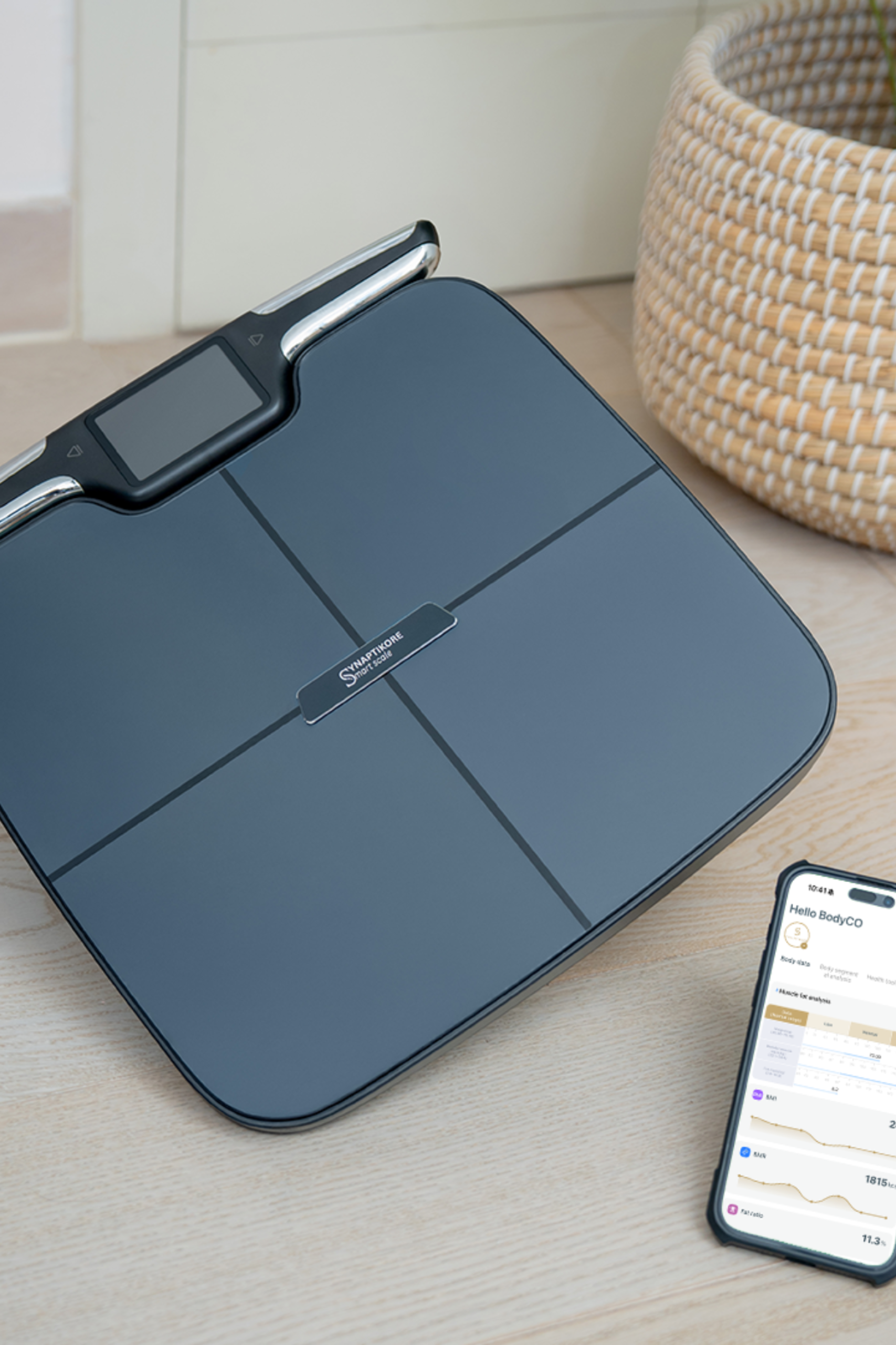 Smart weight scale on a wooden surface with a smartphone displaying app.
