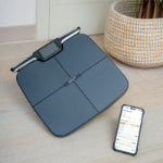 Smart weight scale on a wooden surface with a smartphone displaying app.